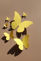 Wall Mural - Yellow paper butterflies on light brown background, top view