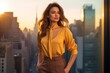 Fashion-forward woman in a golden-yellow blouse and brown slacks posing against an urban cityscape at sunset
