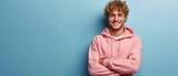 Fototapeta  - Portrait of happy man with curly hair smile toothily keeps arms down wears casual pink hoodie looks cheerful isolated over blue background being in good mood with copy space. Generative ai