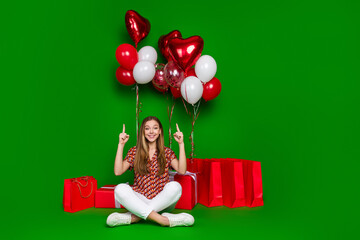 Sticker - Full size photo of cute girl sit near gifts shopping bags indicating up at heart shape air bubbles isolated on green color background