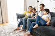 © Vadim Pastuh - Happy family of four using laptop sitting on the sofa in cozy apartment, parents and two kids talking with relatives, spends time on the weekend together at home