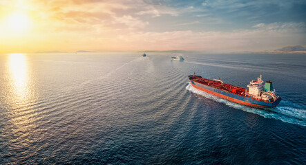 Wall Mural - A group of cargo bulk ships and chemical goods or oil tanker sailing with speed over the ocean into the sunset