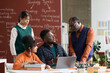 © Mediaphotos - Portrait of senior African American teacher talking to group of students sitting at table with books and computer