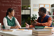 © Mediaphotos - Side view portrait of smiling African American girl talking to senior professor during one on one consultation in college classroom