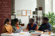 Portrait of senior Black professor talking to group of students sitting at table together in college classroom copy space