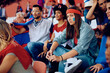 © Drazen - Displeased young woman and her friends watching sports match at stadium.