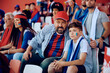 © Drazen - Sports fan and his son watching match from stadium stands.