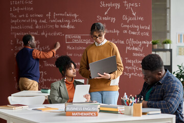 Wall Mural - Team of African American college students doing group study in college classroom with blackboard in background copy space