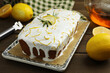 Tasty lemon cake with glaze and citrus fruits on wooden table, closeup