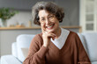 © Home-stock - Portrait of delightful senior woman, resting comfortably on sofa, smiling at camera, creating heartwarming moment of relaxation and joy at home