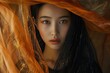 fine art portrait in studio of asian woman in black dress under golden orange veil