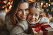 Smiling daughter embracing and leaning on mother's lap near Christmas present at home