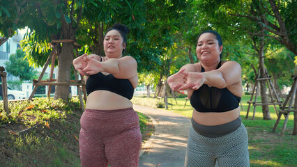 Obese two young asian woman doing stretching arm muscle in the park, woman with overweight warm up and exercise for dieting and health, workout and motivation, oversized and challenge, plus size.