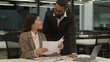 © Yuliia - Asian businesswoman worker Korean female manager woman sorting holding papers document paperwork Arabian businessman Indian leader CEO mentor walk talking two business colleagues in office discuss