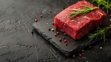  A Piece Of Raw Meat Sitting On Top Of A Cutting Board Next To A Sprig Of Rosemary On Top Of A Piece Of Black Slate With Red Pepper.