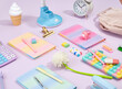 © Dima - Composition of bright office supplies on table. Colorful notebooks, calculator, pencil case pop it, blue table lamp, erasers, white retro alarm clock.