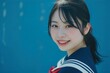 セーラー服を着た笑顔の日本人の女子高生（青背景・卒業・青春・高校生）