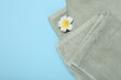 Terry towels and plumeria flower on light blue background, top view. Space for text