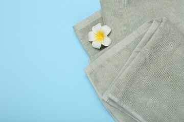 Wall Mural - Terry towels and plumeria flower on light blue background, top view. Space for text