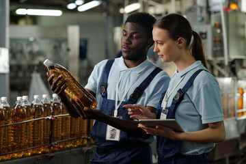 Poster - Young intercultural engineers of quality control looking at plastic bottle containing carbonated lemonade or some other beverage