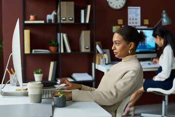 Poster - Side view of young bored African American businesswoman scrolling through online stuff while looking at computer screen