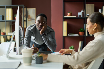 Aufkleber - Young African American businessman bending over workplace of female colleague and looking at her during chat in coworking space