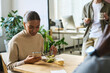 © pressmaster - Young African American female office worker texting in smartphone or watching online video while having vegetarian salad by lunch