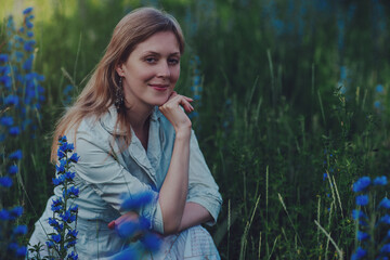 Wall Mural - Portrait of young woman with blue flowers in a field