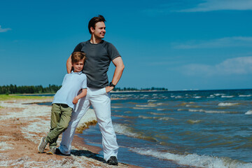 Canvas Print - Happy father and son standing on shore of the lake and looking away