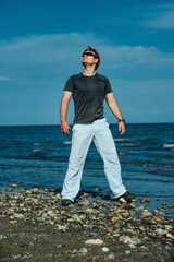 Wall Mural - Young handsome man in sunglasses standing on shore of the lake and looks up