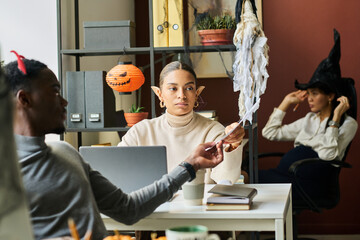 Leinwandbilder - Young African American female economist in Halloween costumes taking financial document from hand of male colleague at meeting