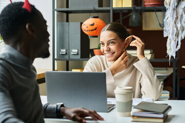 Leinwandbilder - Two happy young office managers or economists in Halloween costumes looking at one another while sitting by desk and having discussion