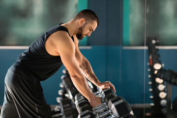 Canvas Print - Sport Equipment Concept. Young Male Athlete Taking Dumbbell From Rack At Gym