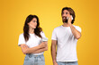 © Prostock-studio - Skeptical woman holding a coffee cup looking at a smiling man talking on a mobile phone