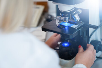  Female scientist using microscope in laboratory.  Biotechnology specialist looking under microscope, doing analysis of test sample. Medical science laboratory: advanced equipment.