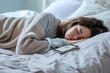 A woman sleeping in bed, next to her mobile phone with a specially installed sleep application, World Sleep Day