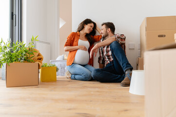 Beautiful young couple expecting a baby just moved into an empty apartment, sitting among cardboard boxes making plans for the future. New beginnings