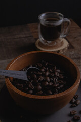 Wooden bowl of coffee beans in a bowl near a cup of coffee