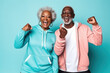 © m - Portrait of Elderly afro-american smiling couple posing raising hands triumphantly over blue background. Mature adults wear activewear sportswear Sport fashion clothes for retired people man and woman