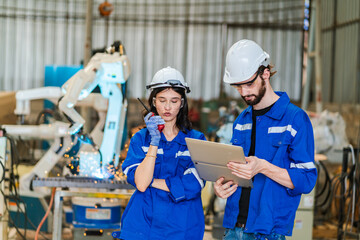 Wall Mural - Artificial intelligence robotic technician concept, Factory engineer inspecting on machine with smart tablet. Worker works at heavy robot arm. Welding with remote system in an manufacturing industrial