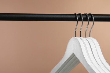 Sticker - Empty clothes hangers on rack against light brown background, closeup. Space for text