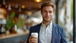 A young handsome businessman is holding a paper glass of coffee in his hands