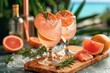 Refreshing and elegant, two glasses of pink bellinis adorned with citrus slices and fragrant rosemary sit atop a rustic wooden board, inviting you to indulge in a classic cocktail experience amidst t