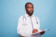 African american medic practitioner grasping a clipboard while gazing at the camera. Black male medical resident holding patients charts and documents while standing against isolated background.