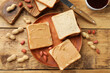 Tasty peanut butter sandwiches and peanuts on wooden table, flat lay