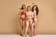 © Velista production - Female solidarity. Full size of barefooted laughing woman in bikini posing together in studio with beige background. Three caucasian women having different hairstyle and body shape.