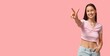 © Pixel-Shot - Sexy young woman with navel piercing showing victory gesture on pink background with space for text
