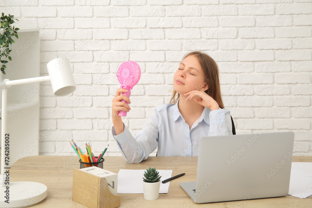 Beautiful young woman with handheld mini fan in office