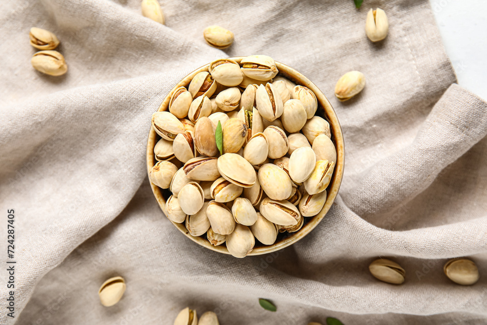Bowl with tasty pistachio nuts on white background