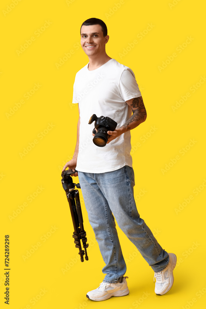 Male photographer with modern camera and tripod on yellow background